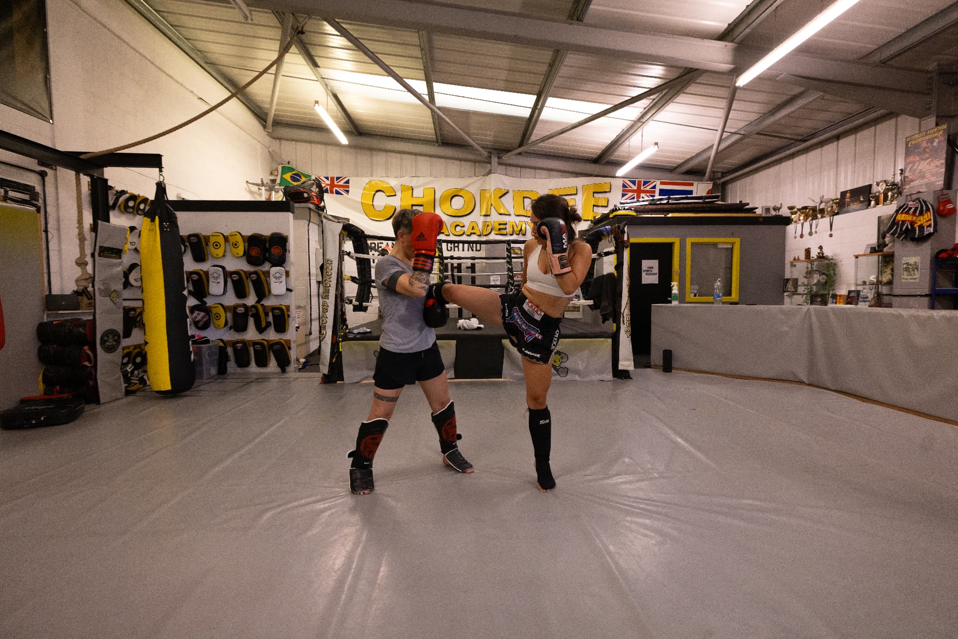 Member throwing a high kick on pads under the Chokdee Academy banner