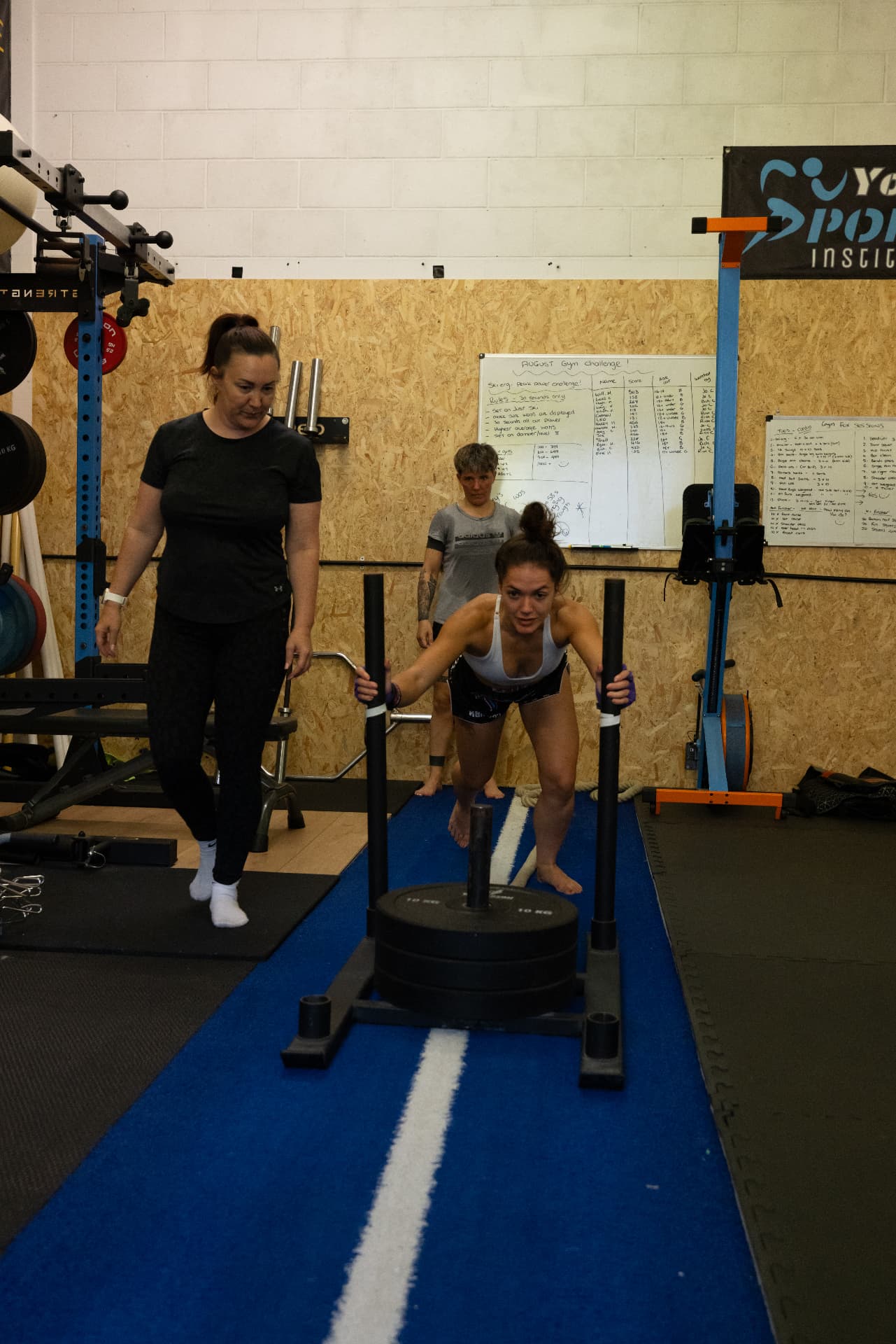 Member pushing a weighted sled along the blue turf strip